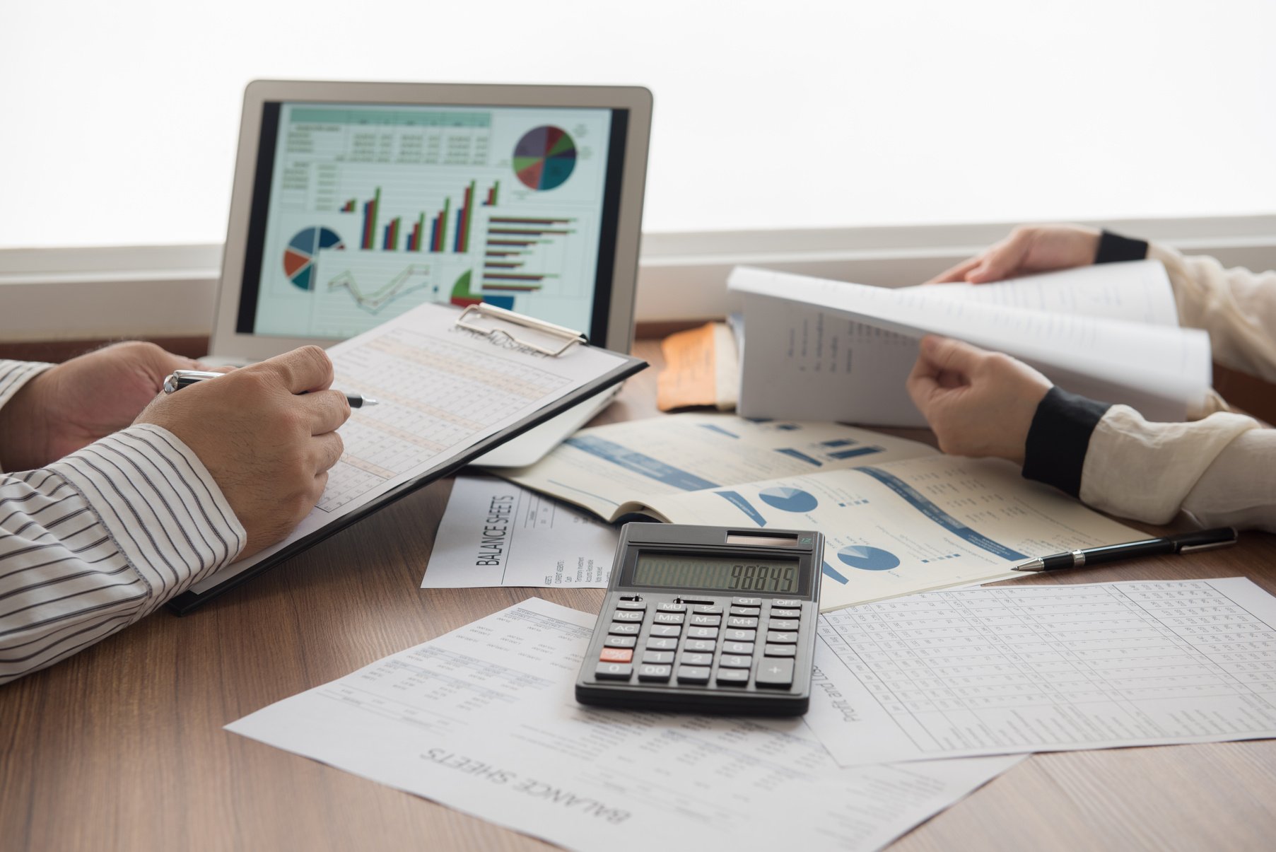 two people sitting at a desk with papers and a calculator